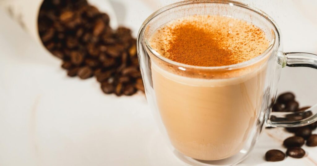  A cup of golden milk, a warm beverage made with turmeric, milk, and spices, garnished with a sprinkle of cinnamon.