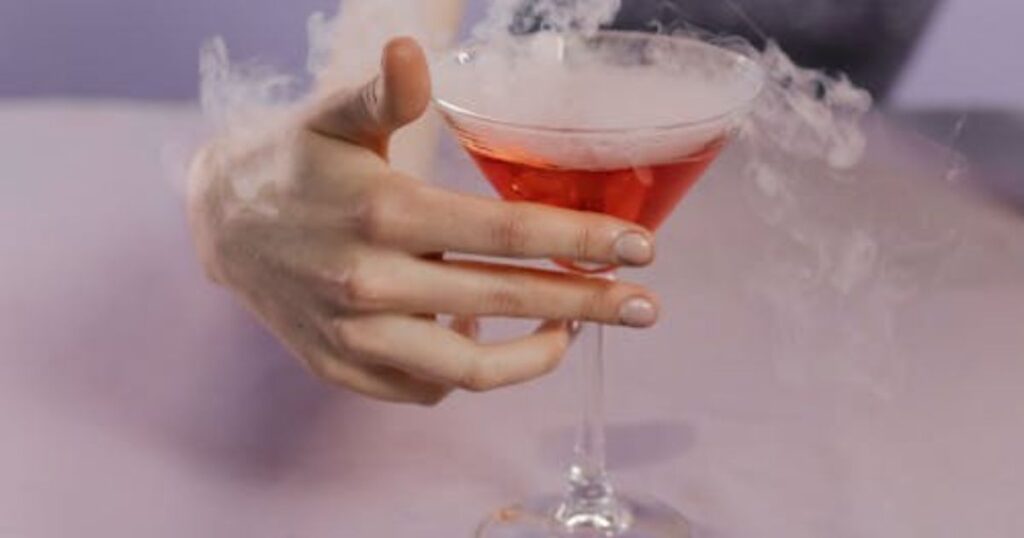 presents a glass of espresso martini, steam billowing from it, emphasizing an elegant serving style.