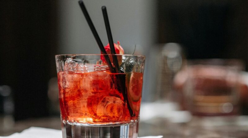 A vibrant blood orange negroni in a glass, featuring a slice of blood orange, set against a rustic wooden background.