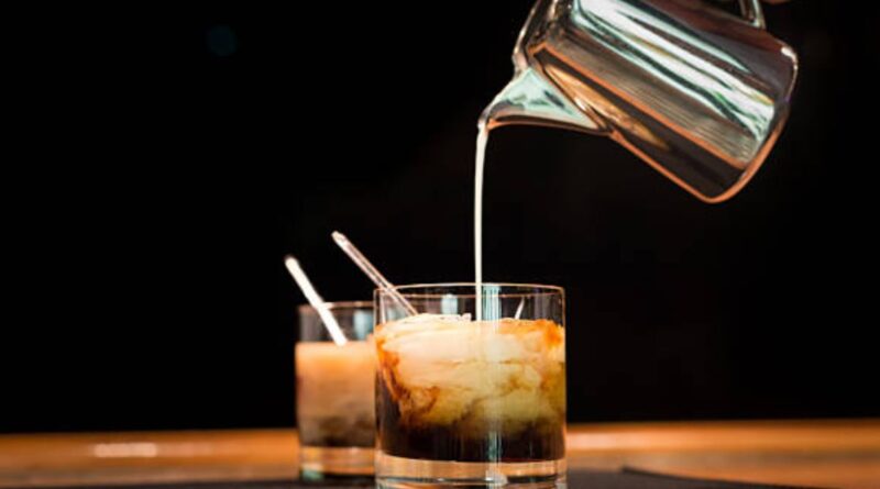 Ice is being poured into two glasses of iced coffee, illustrating the steps for making a Cutwater White Russian.
