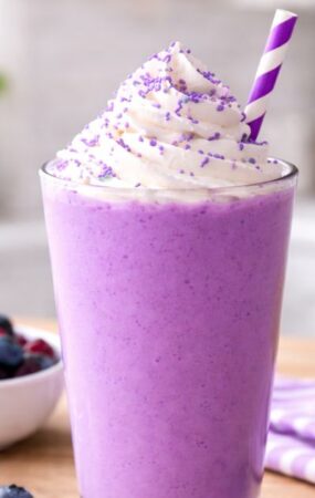 purple smoothie topped with whipped cream and fresh berries, featured in the Grimace Shake Recipe.