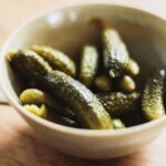 A cup filled with pickles sits on a table, showcasing the vibrant green color and briny texture of the pickles inside.