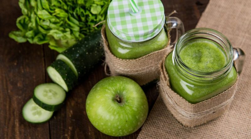 Green smoothie with cucumber and apple on a wooden table, featured in a guide on making weight loss smoothies.