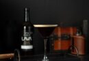 A dark espresso martini on a tray beside a bottle of whiskey, showcasing a stylish drink presentation.