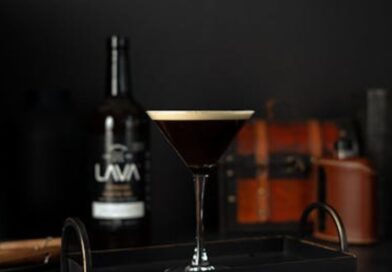 A dark espresso martini on a tray beside a bottle of whiskey, showcasing a stylish drink presentation.