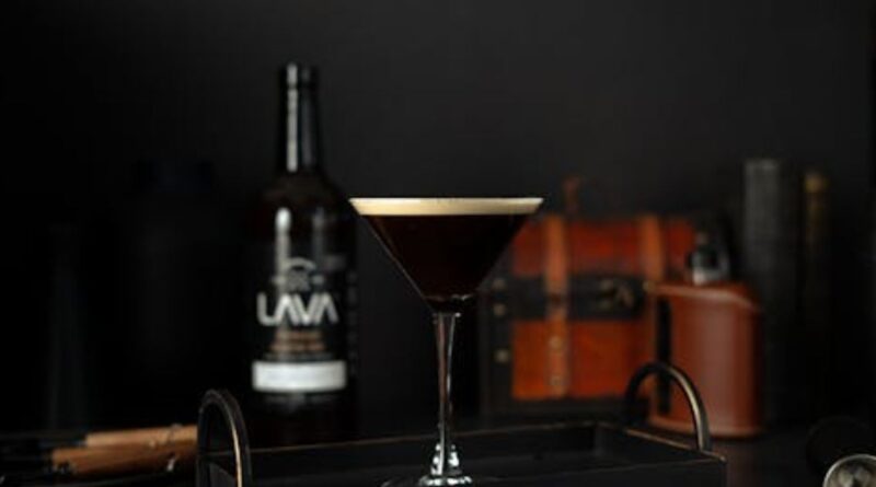 A dark espresso martini on a tray beside a bottle of whiskey, showcasing a stylish drink presentation.