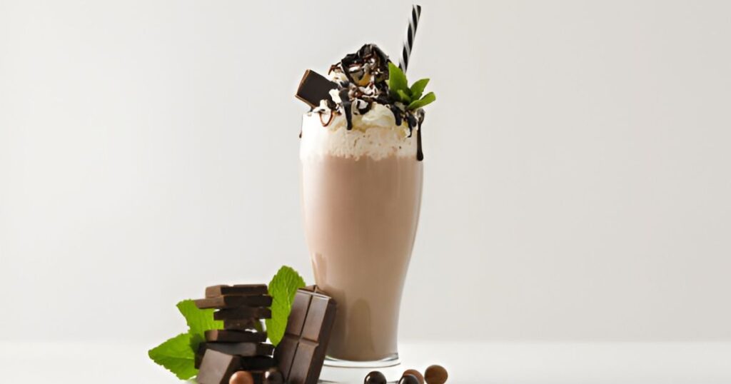 A tall glass of chocolate milkshake topped with fresh mint leaves, representing indulgence and high calorie content.

