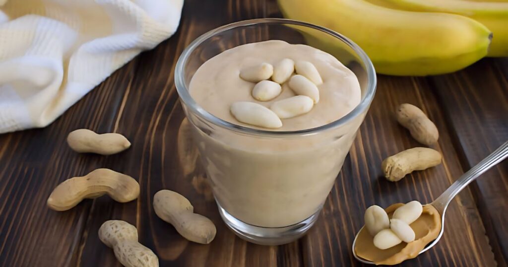 A glass filled with a thick peanut butter and banana smoothie, garnished with a slice of banana on the rim.