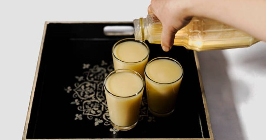 A person pours orange juice into three clear glasses on a table.