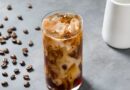 Iced coffee in a glass with coffee beans scattered around, illustrating a homemade cold brew coffee recipe.