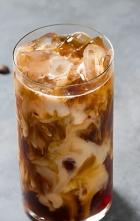 Iced coffee in a glass with coffee beans scattered around, illustrating a homemade cold brew coffee recipe.