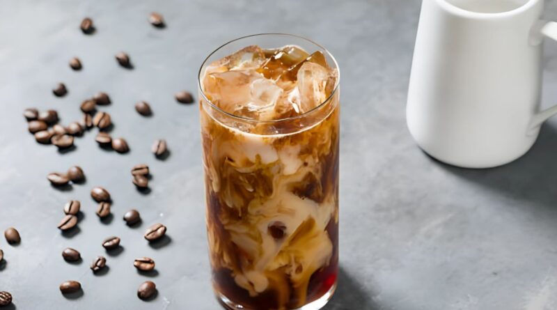 Iced coffee in a glass with coffee beans scattered around, illustrating a homemade cold brew coffee recipe.