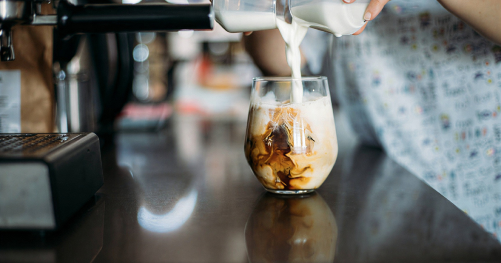 A person adds milk to a glass of cold brew coffee, showcasing a method for making cold brew coffee at home.