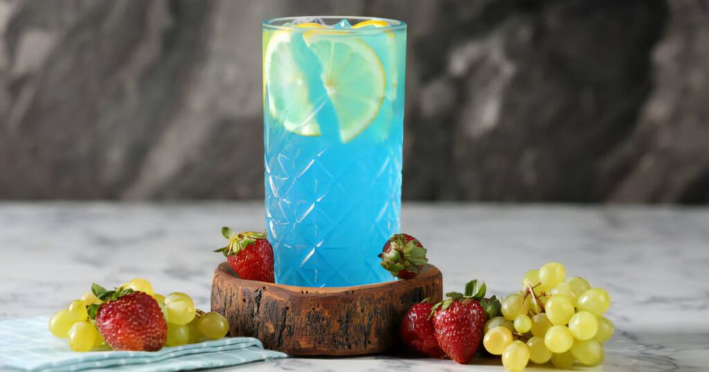A vibrant blue drink garnished with fresh strawberries and grapes, illustrating how to make sonic ocean water