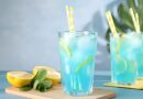 Glass of blue lemonade with straws and lemon slices, illustrating a sweet and refreshing drink recipe.