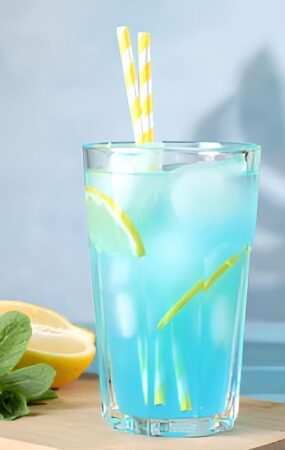 Glass of blue lemonade with straws and lemon slices, illustrating a sweet and refreshing drink recipe.