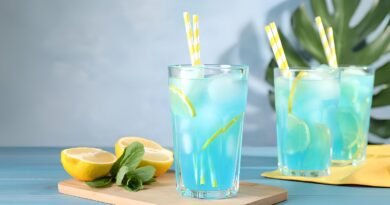 Glass of blue lemonade with straws and lemon slices, illustrating a sweet and refreshing drink recipe.
