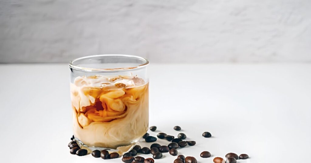 Cold brew coffee served in a glass with coffee beans on a white background, highlighting its refreshing appearance.