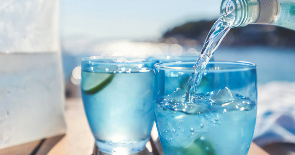 Blue drink being poured into two glasses on a wooden table, showcasing a refreshing beverage experience.
